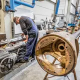 A man working on a lathe machine and with a shaft behind him