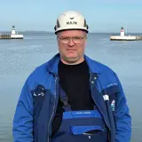 Man in blue jacket and white helmet in front of lighthouse