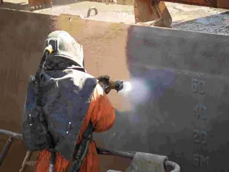 A person grit blasting a ship hull