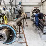 An engine shaft and a man working on a lathe machine 